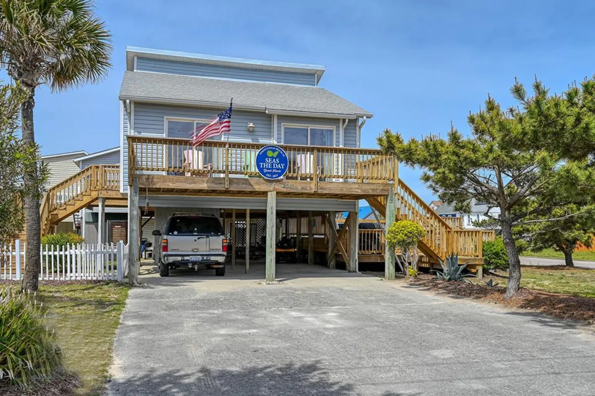 This exterior shot shows the driveway in front of the house, bordered by palm trees, with a visible house sign and a wooden deck above. The ample driveway highlights the space available for multiple vehicles, and the arrangement of the entry area suggests secure, convenient access to the home.