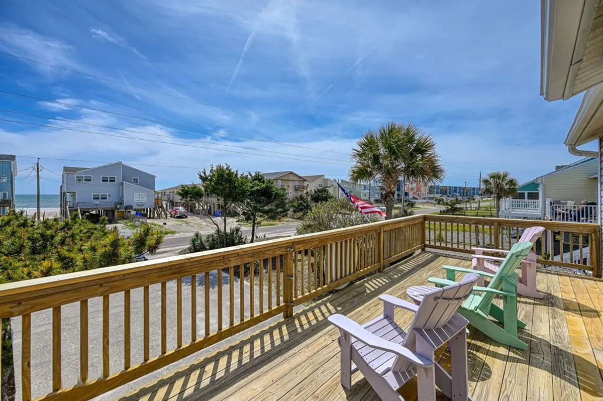 This image features colorful Adirondack chairs arranged on a sun deck with palm trees and a stunning distant ocean view beneath a blue sky. The setup invites relaxation and socialization, perfectly capturing the indoor-outdoor lifestyle described in the section.