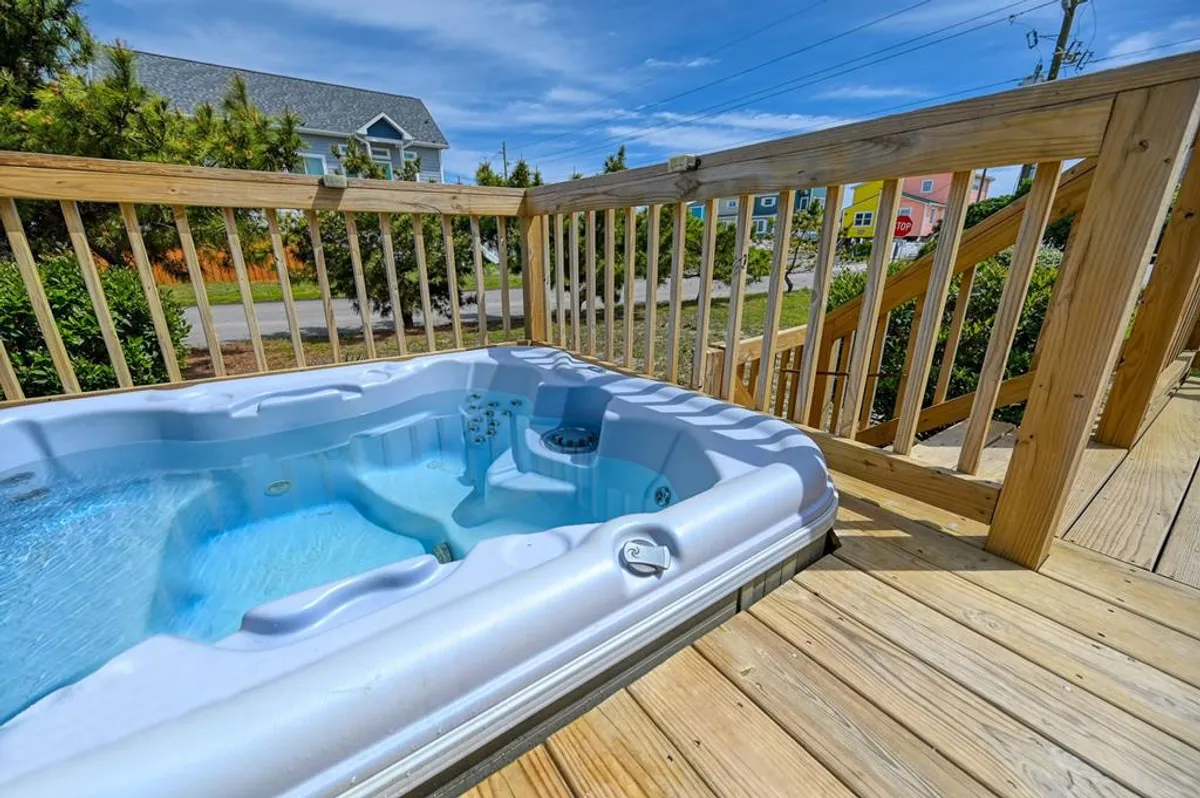 A tranquil hot tub set on a wooden deck, surrounded by lush greenery and open sky. The ambiance is peaceful, inviting guests to relax and soak while enjoying sunset views.