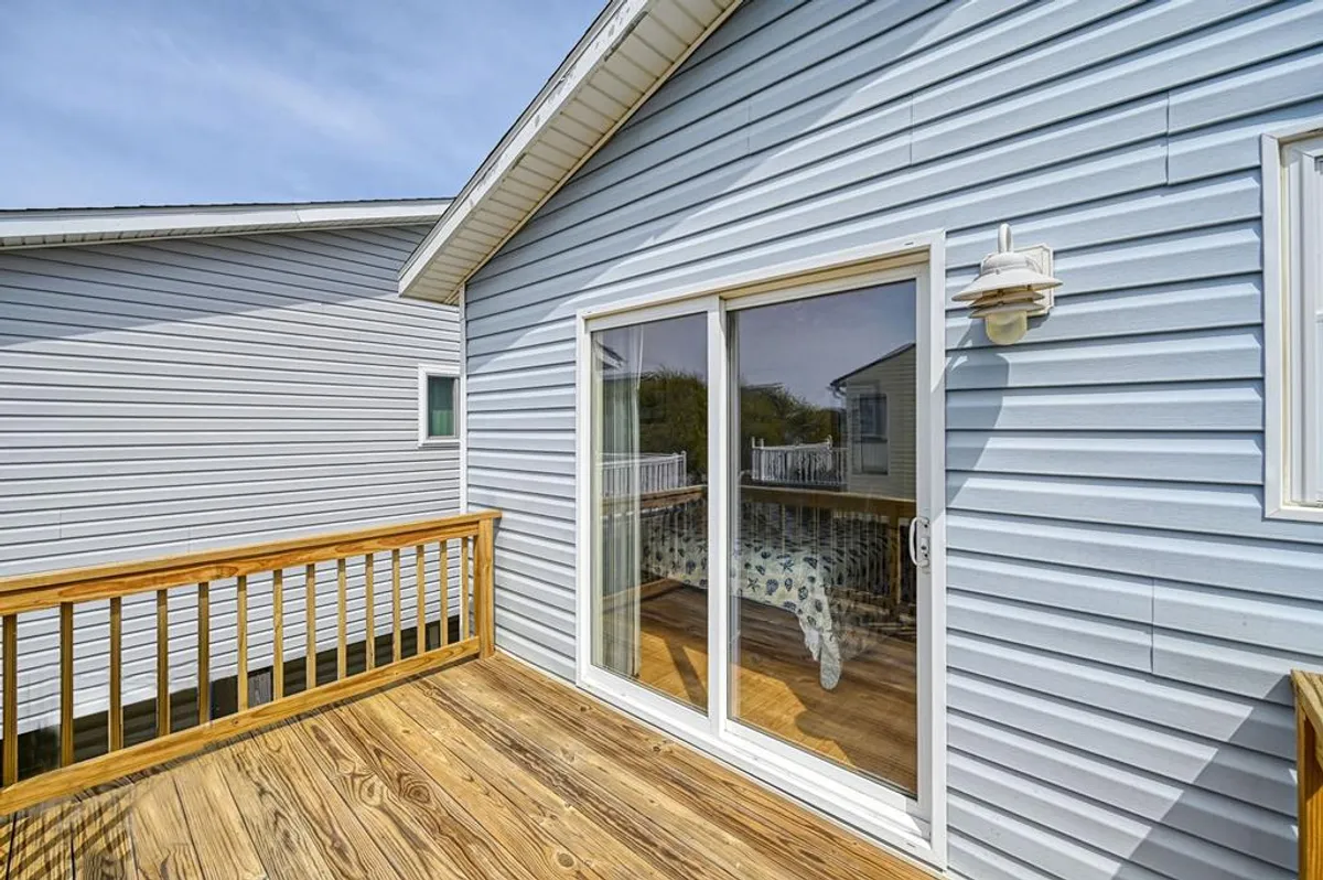 A cheerful wooden deck adjoins a home with blue siding and a sliding glass door. The space feels open and inviting, ideal for both humans and pets, and is perfect for morning coffee or playtime. The fenced area is visible, suggesting a secure space for pets to roam.