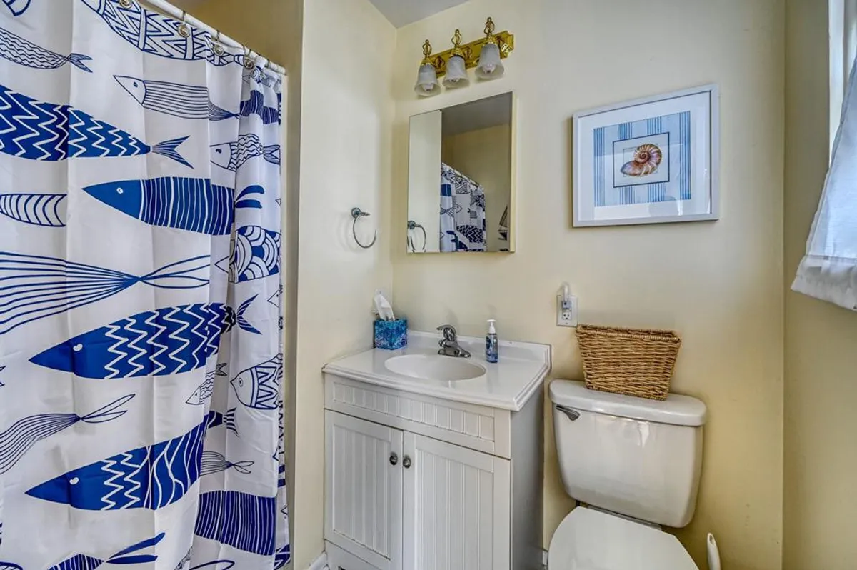 A cheerful bathroom with a fish-themed shower curtain, a vanity with sink and mirror, and framed artwork. The space is playful yet functional, with nautical details that tie into the overall decor.
