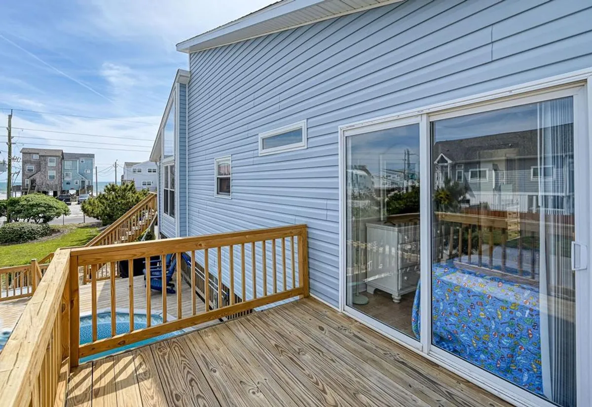 An exterior view of a deck with a railing, window views, and glimpses of colorful bedding inside. The scene feels casual and cheerful, ideal for enjoying the outdoors, sharing meals, or taking in sunset views.