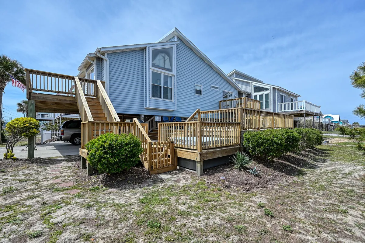 A welcoming exterior shot of a wooden deck with stairs, surrounded by lush greenery and windows overlooking the area. The deck looks ready for gatherings or outdoor relaxation, and its open, fenced feel implies a safe space for pets to enjoy the outdoors with their owners.