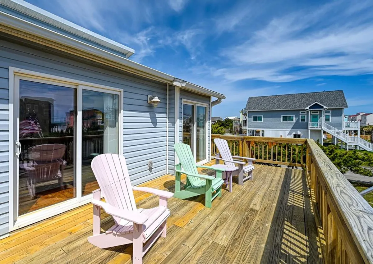 This image showcases a cheerful exterior deck featuring colorful Adirondack chairs set against a blue sky and with views of surrounding homes. The deck is inviting, spacious, and perfect for relaxing outdoors, socializing, or enjoying the fresh coastal air.