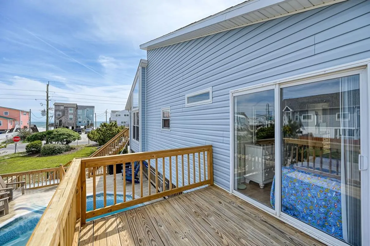 A cheerful exterior shot showing a wooden deck overlooking a private pool and a view of the quiet street and neighboring houses. The setup suggests a welcoming space for relaxing by the pool, enjoying the view, and gathering with family or friends.